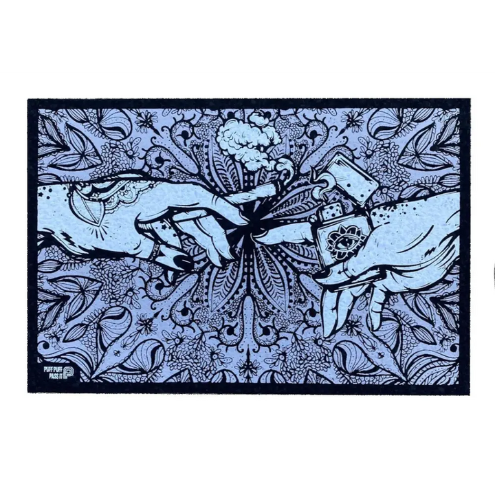 A rectangular mat featuring an intricate illustration of two hands, one holding a lit cannabis joint and the other holding a lighter with an eye symbol, against a detailed floral and paisley background in light blue and dark blue.