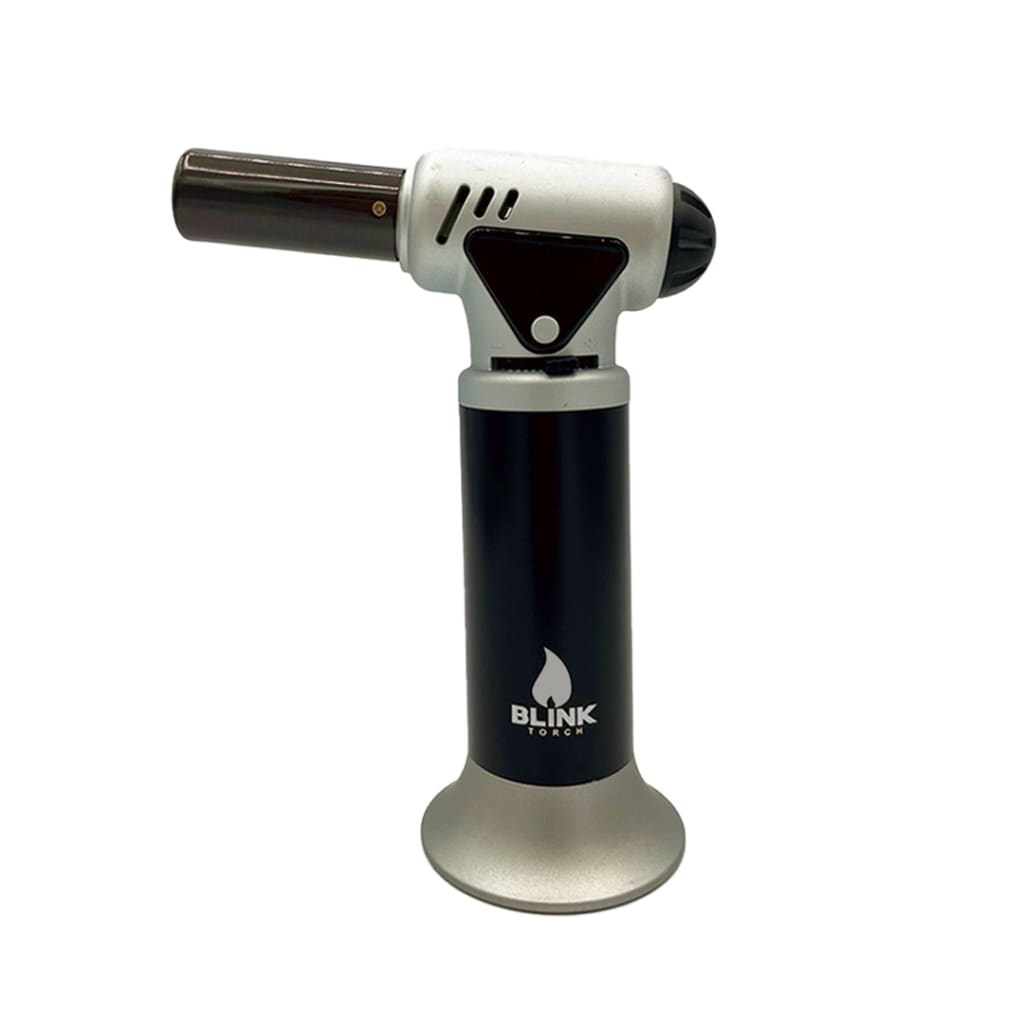 A black and silver handheld butane torch standing upright on a white background. The torch features a black body with a 'Blink Torch' logo and a silver base and top section, including the nozzle and handle.