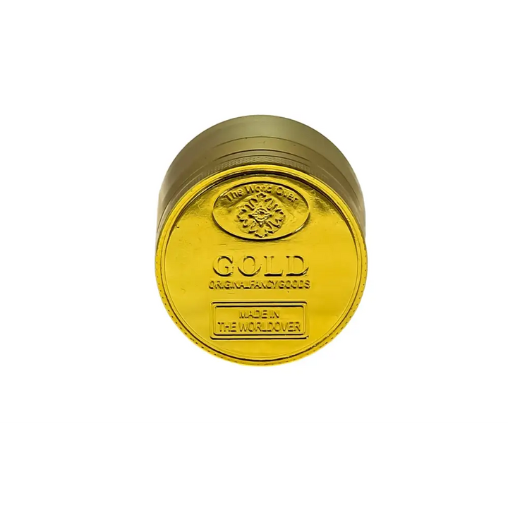 Close-up view of the shiny gold top of a cylindrical herb grinder, featuring embossed text that reads 'GOLD ORIGINAL FANCY GOODS' and 'MADE IN THE WORLDOVER' with a small floral emblem.