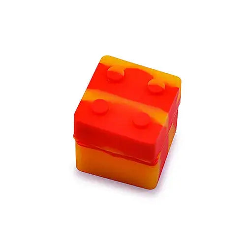 Angled close-up of a small, rectangular silicone container with swirled orange and yellow colors, featuring four studs on its top surface, resembling a building block.