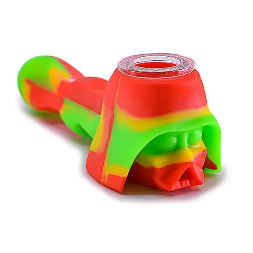 Close-up of a vibrant red, green, and yellow silicone hand pipe shaped like a space villain's helmet, featuring a clear glass bowl insert at the top.