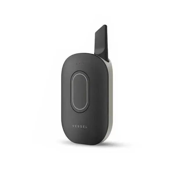 Close-up, slightly angled view of a dark grey, oval-shaped vaporizer battery with a silver side panel and a black cartridge mouthpiece extending from the top. The 'VESSEL' logo is visible at the bottom.