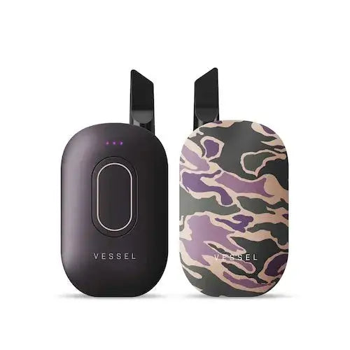 Two compact, rounded rectangular vaporizers standing upright side-by-side, one in solid black and the other in a purple and tan camouflage pattern.