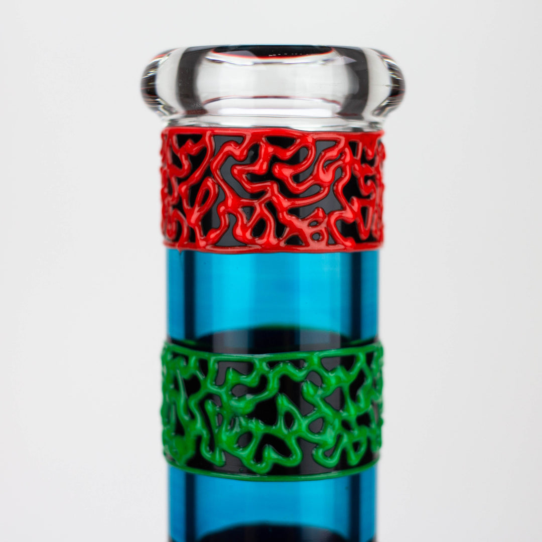 Close-up detail shot of the neck of a blue glass water pipe, featuring a clear glass mouthpiece and two textured bands in red and green with an organic pattern.