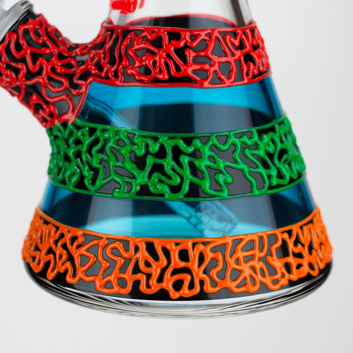 Close-up detail of a clear glass beaker water pipe with vibrant red, green, and orange abstract patterns on black bands, filled with blue liquid.