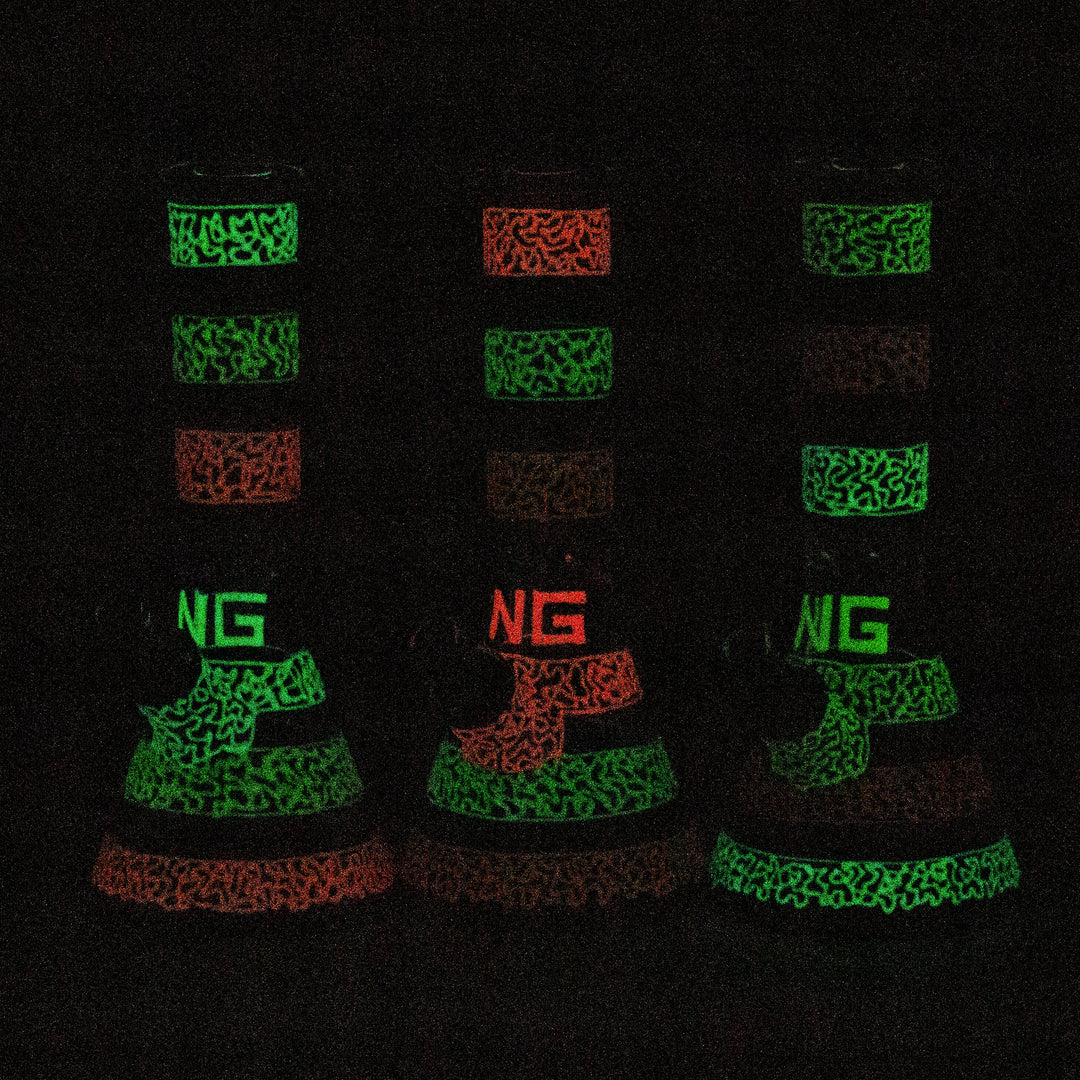 Three glow-in-the-dark beaker bongs, two with green glowing patterns and one with orange glowing patterns, against a dark background, showcasing their illuminated designs.